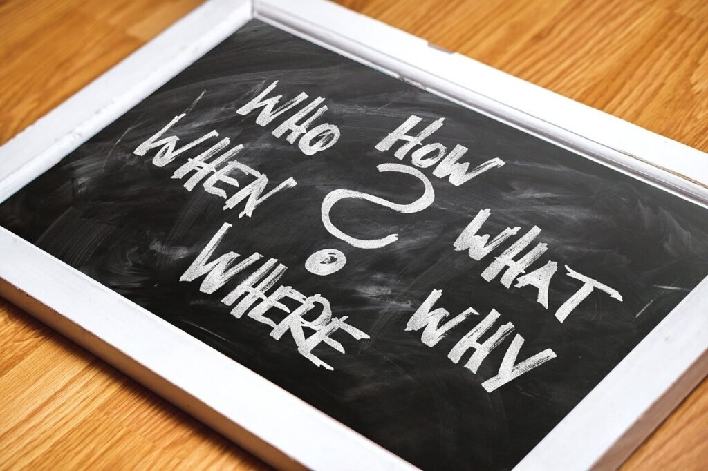 Chalkboard with handwritten white text displaying question words who, how, what, where, and why.